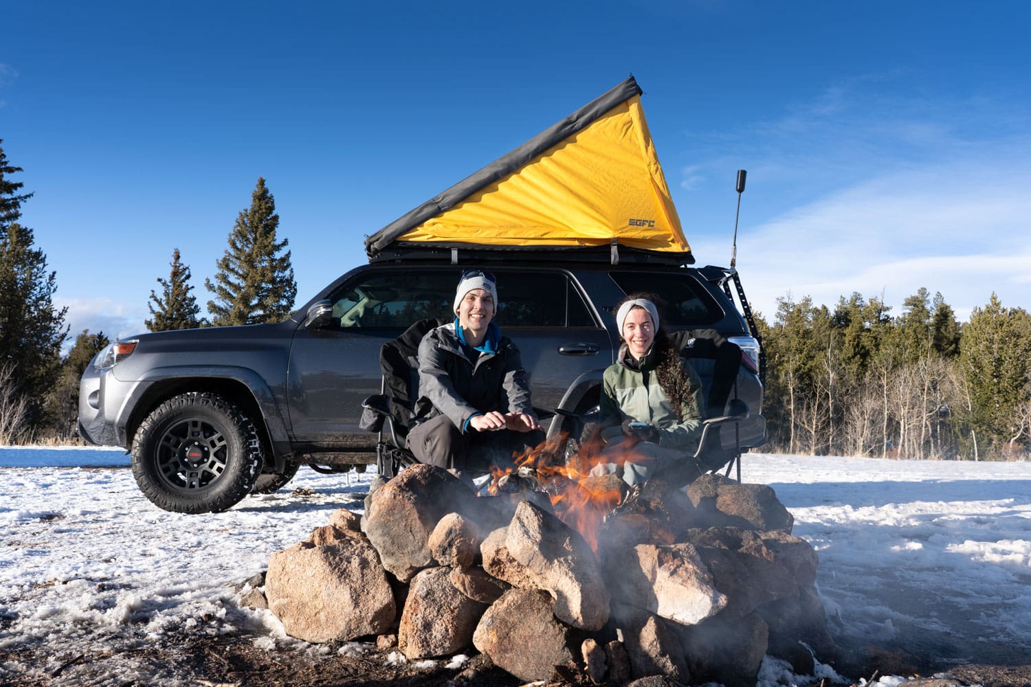 Man and woman sitting in front of an SUV and a fire pit